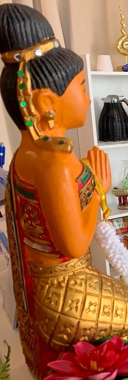 Statue thaïe en posture de wai, mains jointes, une guirlande de jasmin entre les mains